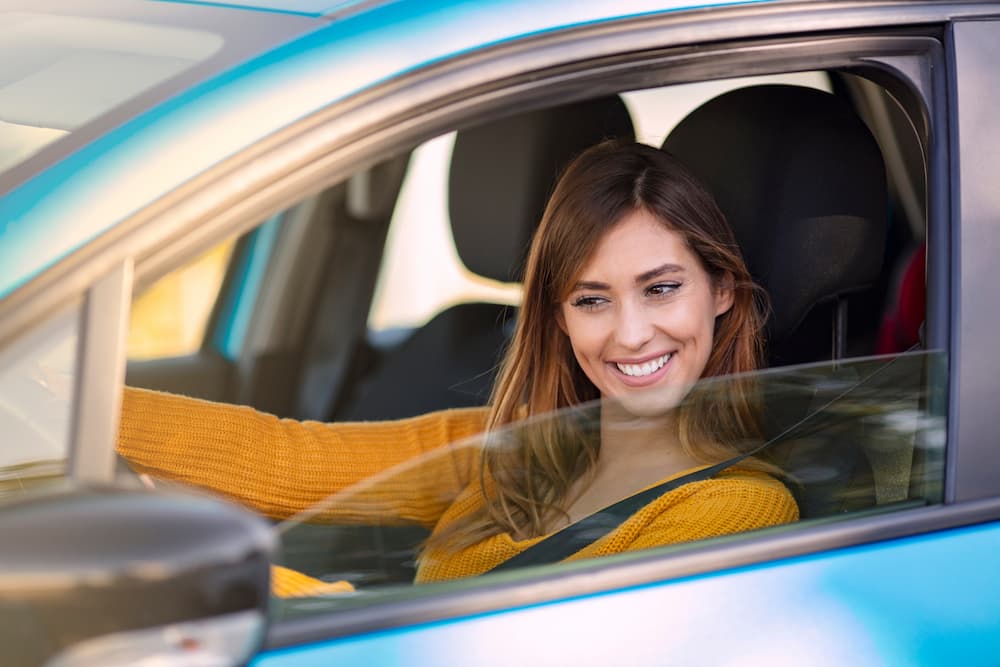 A young woman sits in her new car from Cactus Auto smiling