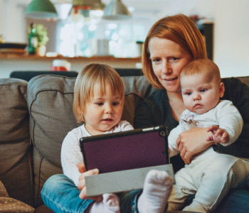 woman holding a tablet with two babies on a couch